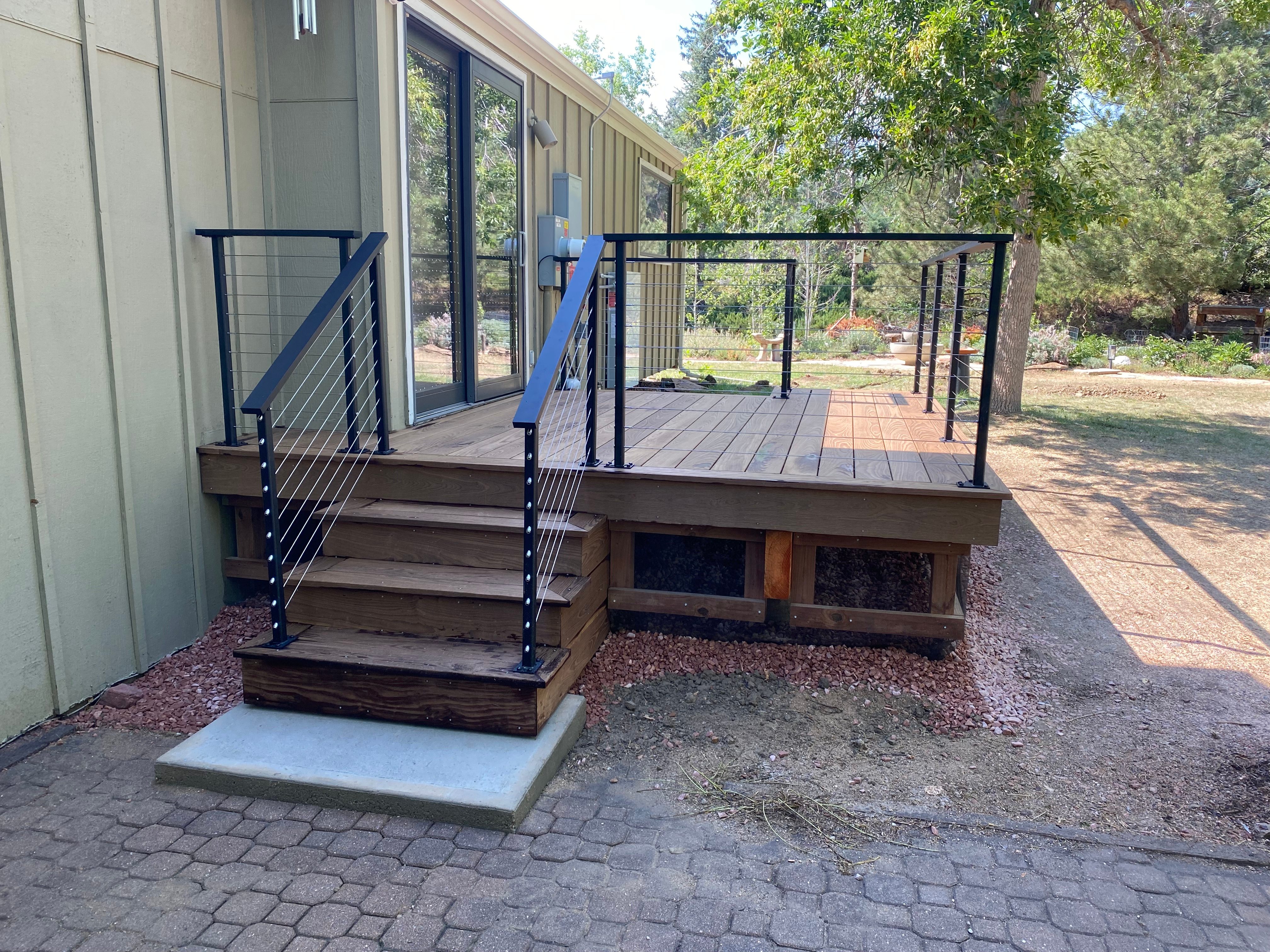 Deck stairs with black steel handrail leading to paver patio