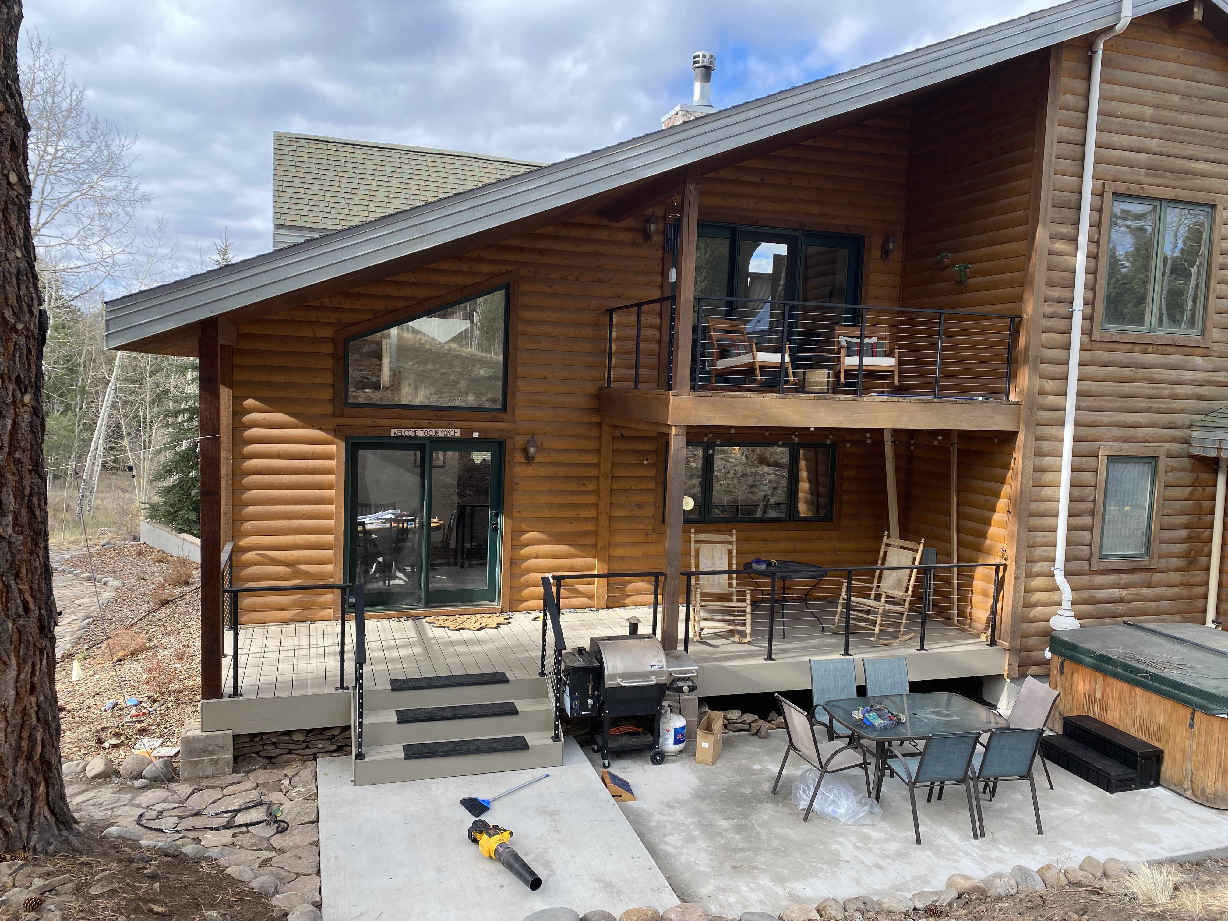 Rear elevation of a log home with a rebuilt deck, new patio and hot tub pad
